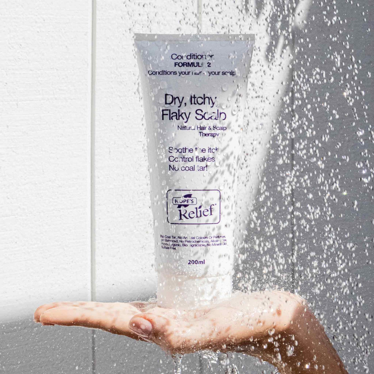 Hand holding a bottle of 'Dry, Itchy Flaky Scalp' treatment under running water.