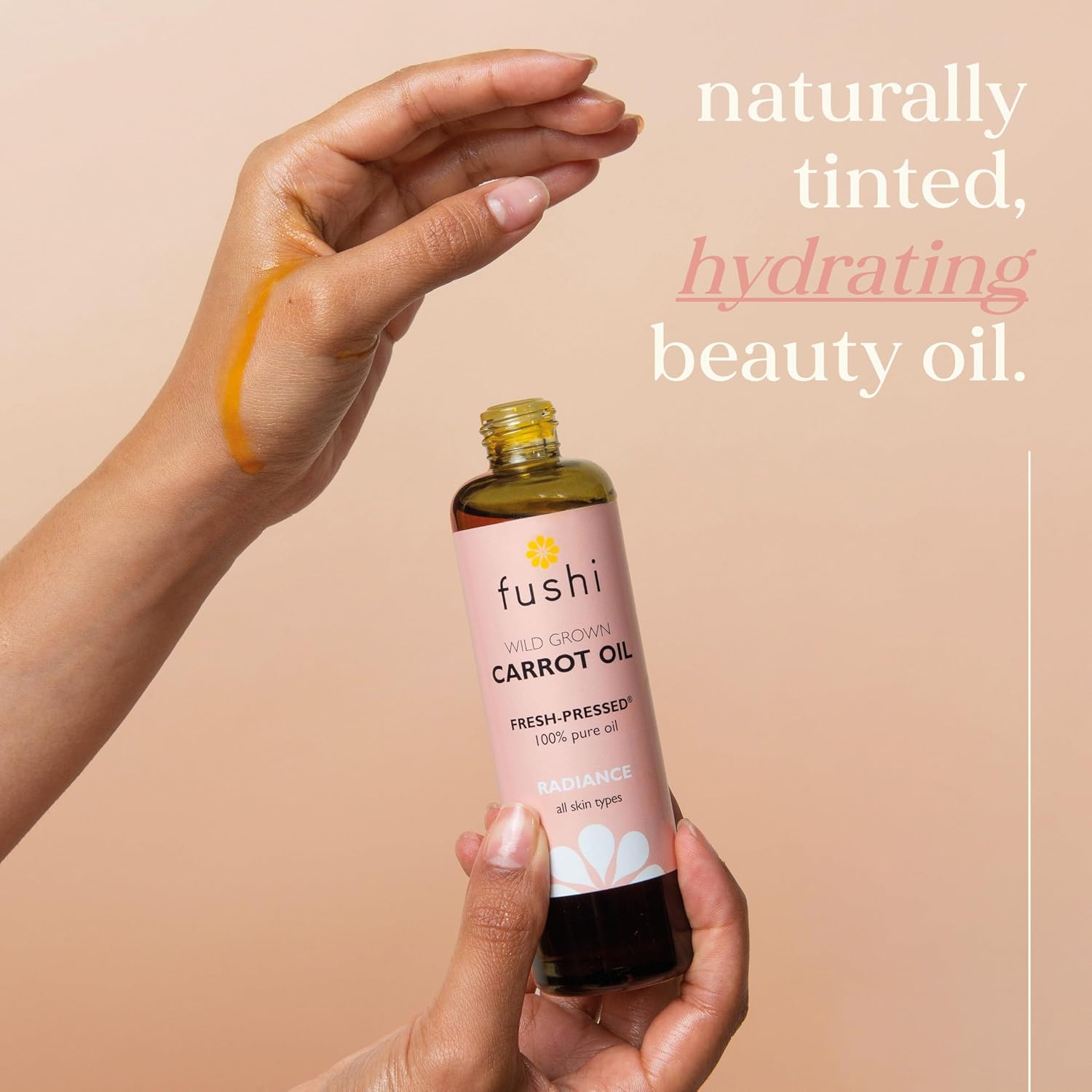 Fushi carrot oil bottle held by a hand with a beige background