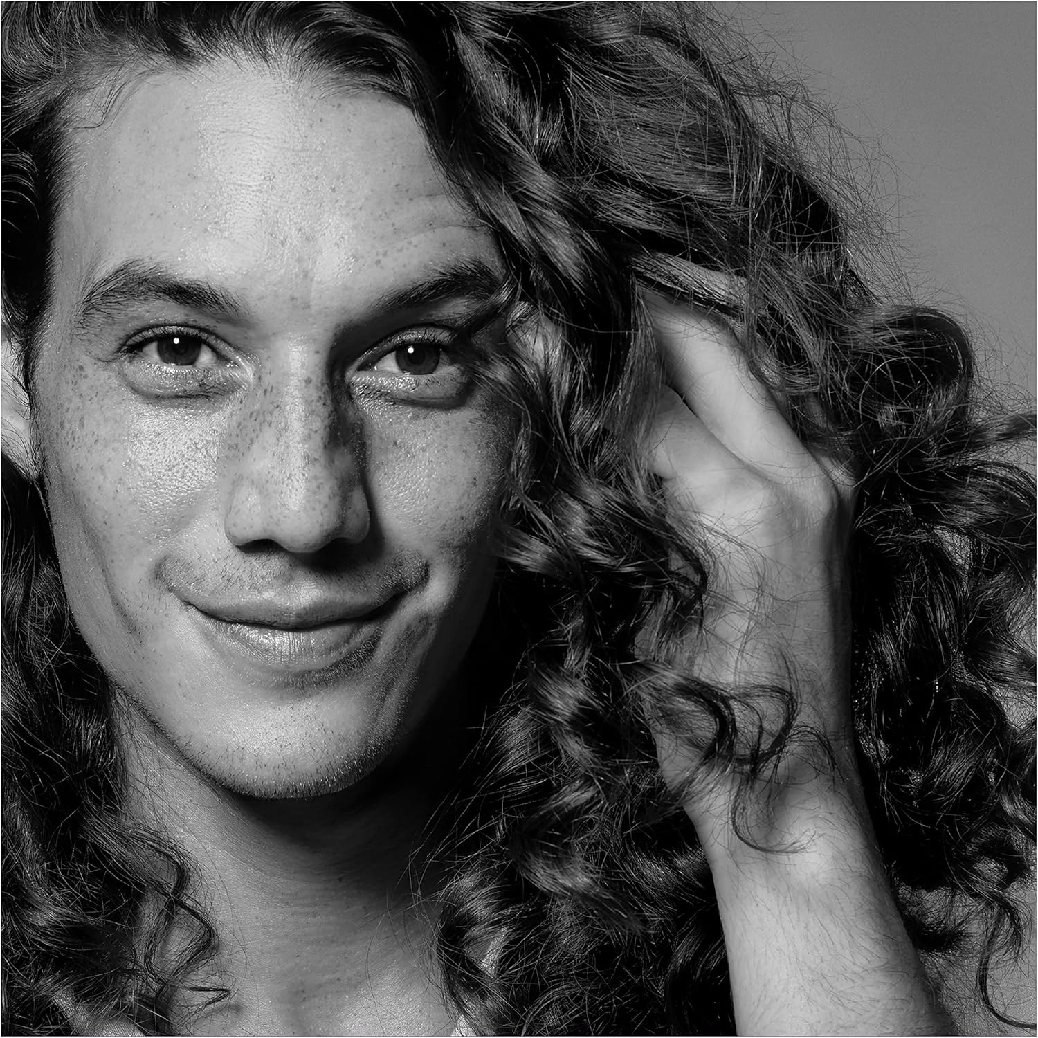 Black and white portrait of a person with curly hair, one hand on their face.