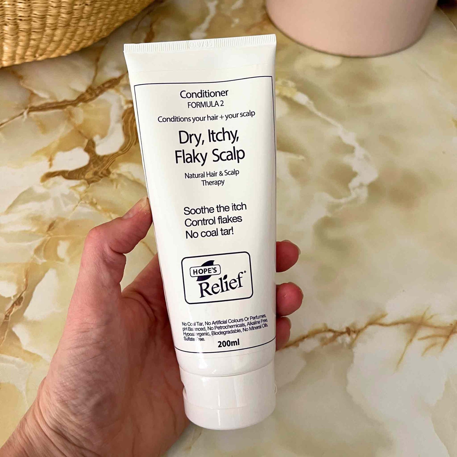 Hand holding a tube of Hope's Relief conditioner on a marble surface