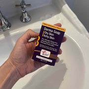 Hand holding a box of Derma-Soap in front of a sink