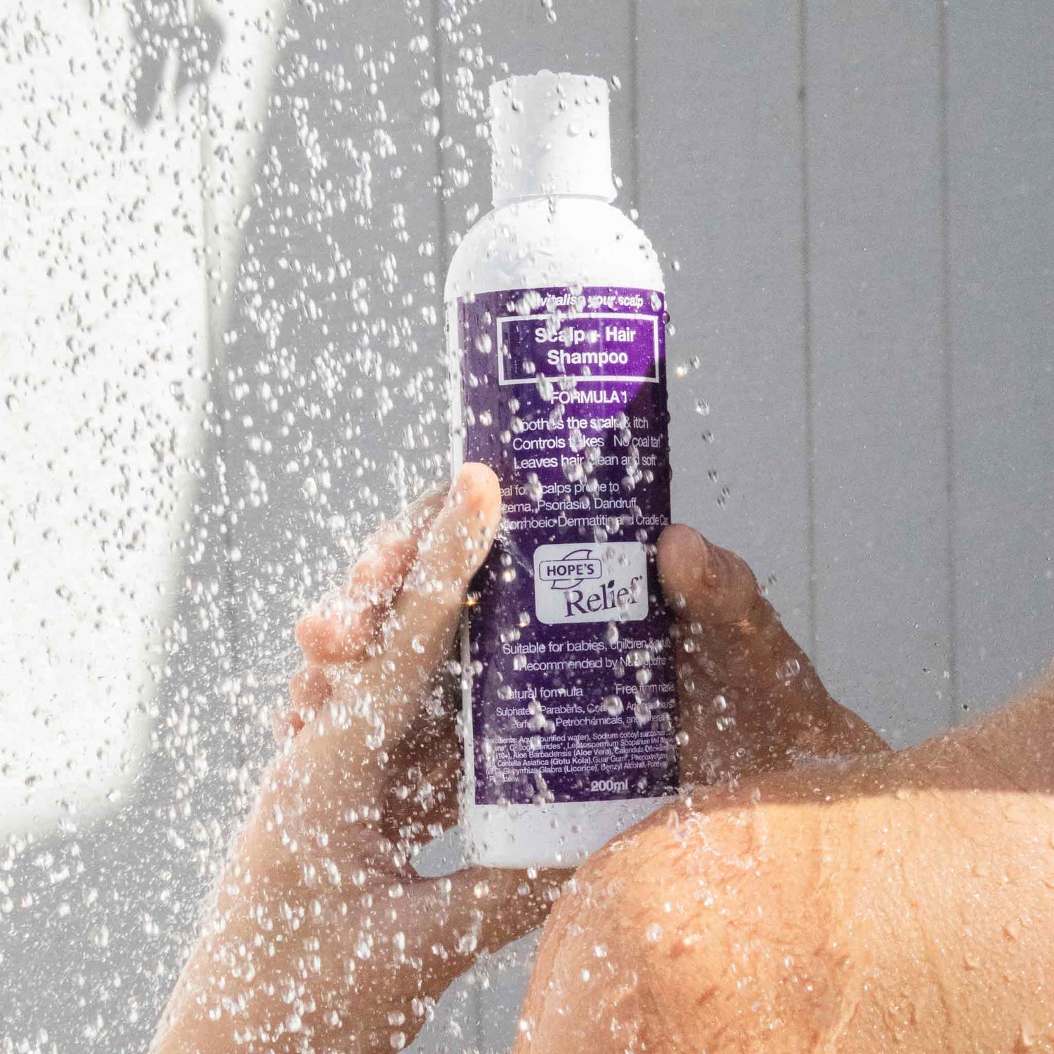 Person holding a bottle of shampoo under running water
