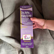 Hand holding a box of Hopes Relief shampoo for dry, itchy, flaky scalp on a gray fabric background.