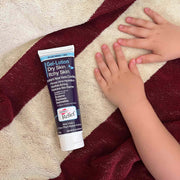 Tube of Aveeno Relief Gel-Lotion for dry skin on a textured surface with hands touching the fabric.