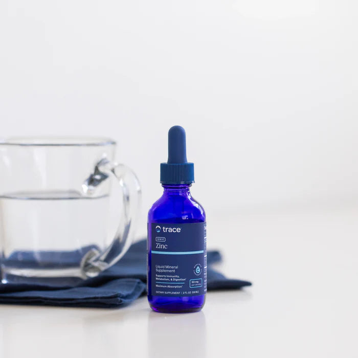Blue bottle of trace minerals supplement with dropper next to a clear glass mug on a white surface.