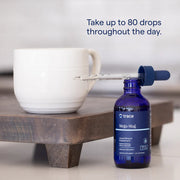 Blue bottle of trace Mega-Mag supplement with dropper next to a white mug on a wooden surface.