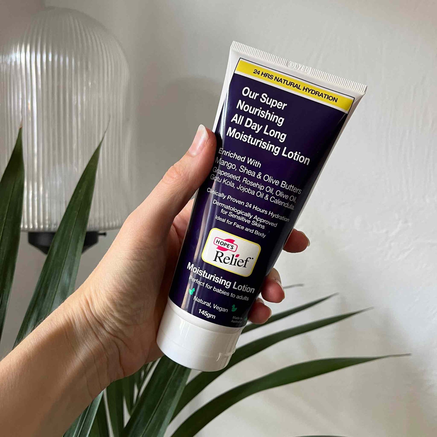 Hand holding a tube of L'Occitane Relief Moisturising Lotion with a plant in the background