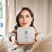 Woman holding a skincare product with 'ReSens' branding in a cozy indoor setting.
