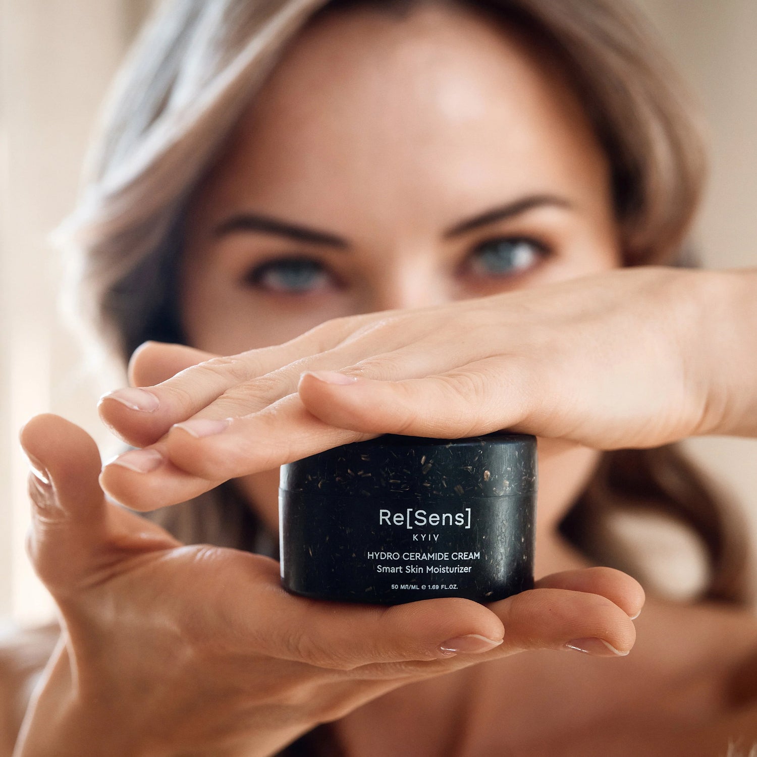Woman holding a jar of Re[Sens] cream in front of her face