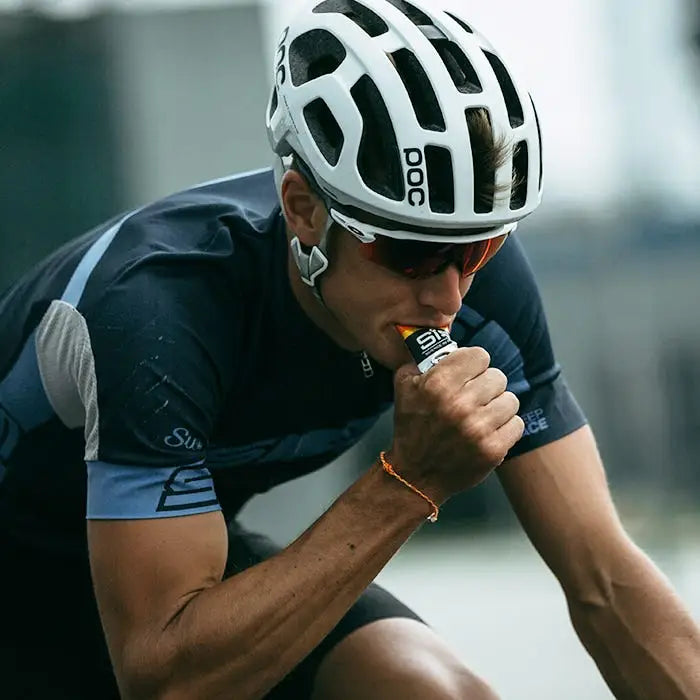 Person consuming SIS Orange energy gel from sachet during activity.