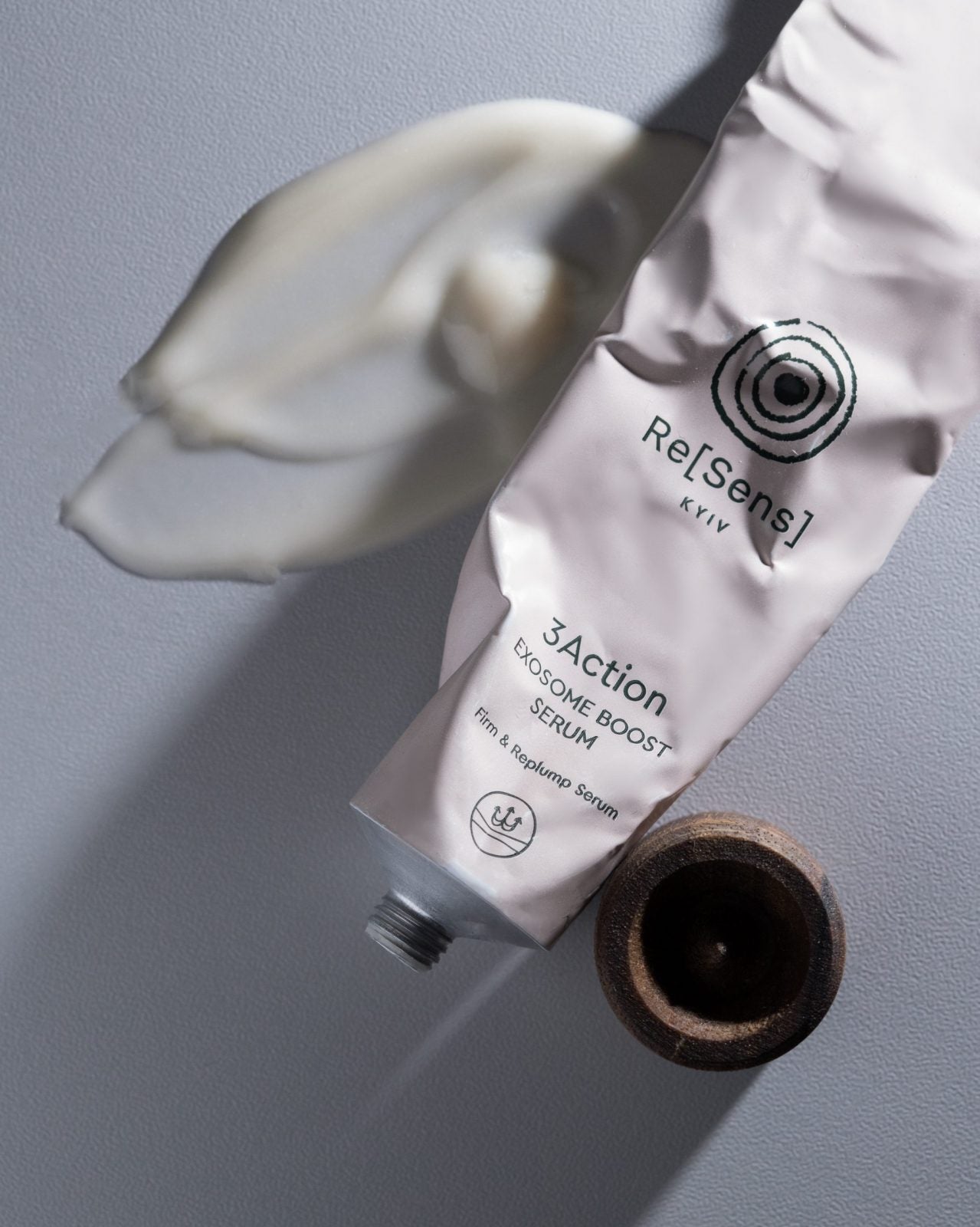 Tube of Re[Sens] 3Actionosome Boost Serum with a wooden applicator on a gray background