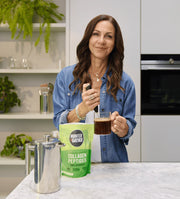 Woman in a kitchen holding a bag of Hunter Gather Collagen Peptides and a glass of liquid.