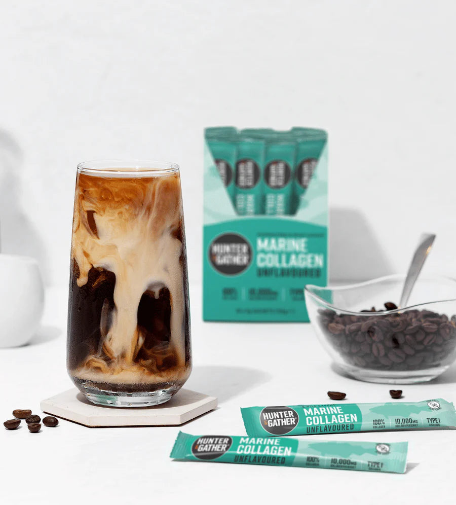 Glass of iced coffee with Hunter Gather Marine Collagen Unflavored packets and a bowl of chocolate chips on a white background.